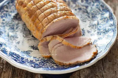 Arrosto di maiale morbido con sughetto, affettato su un piatto decorato con motivi blu. Perfetto per un pranzo domenicale.
