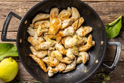 Pezzetti di petto di pollo dorati in padella, conditi con limone e erbe aromatiche. Un'idea veloce per le tue ricette di petto di pollo.