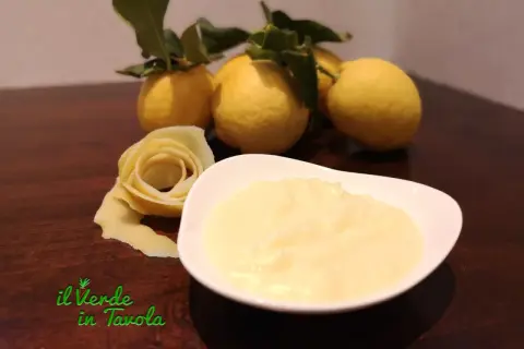 Una ciotola di cremosa crema al limone, con limoni freschi e una decorazione a forma di rosa fatta con la scorza.