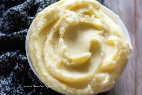 Una ciotola di cremoso pure di patate, guarnito con pepe nero macinato, su un tessuto scuro.