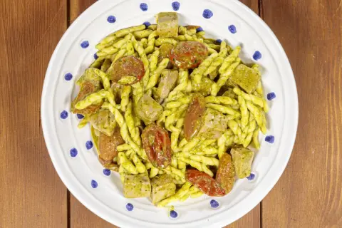 Piatto di trofie alla carlofortina con tonno, pomodorini secchi e pesto, servite su un piatto bianco con decorazioni blu.