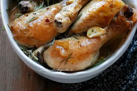 Cosce di pollo succulente, dorate e profumate al rosmarino e aglio, servite in una ciotola bianca.