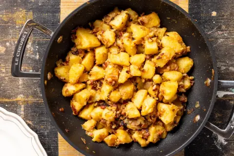 Patate in tecia dorate e croccanti, con pezzetti di pancetta e cipolla, pronte per essere gustate.