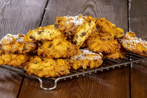 Biscotti croccanti, simili a rose del deserto, con uvetta e fiocchi di mais, spolverati di zucchero a velo su una griglia metallica.