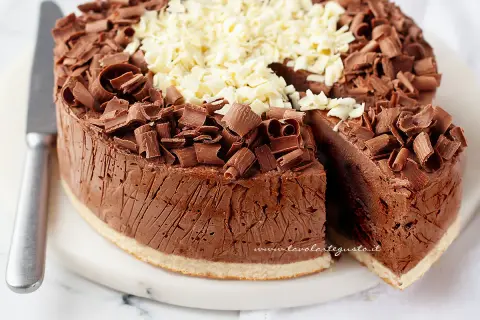 Delizioso semifreddo al cioccolato, ricoperto di riccioli di cioccolato fondente e bianco. Una fetta è stata tagliata, rivelando la sua consistenza cremosa.