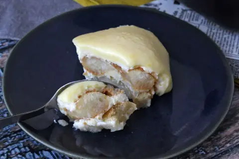 Una fetta di tiramisù al limone su un piatto blu, con un cucchiaino che ne preleva un assaggio.