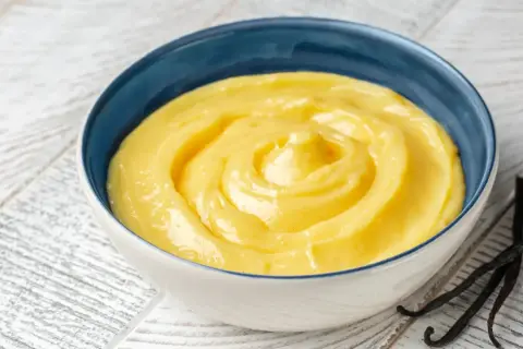 Una ciotola di cremosa crema pasticcera classica, con baccelli di vaniglia scuri accanto.