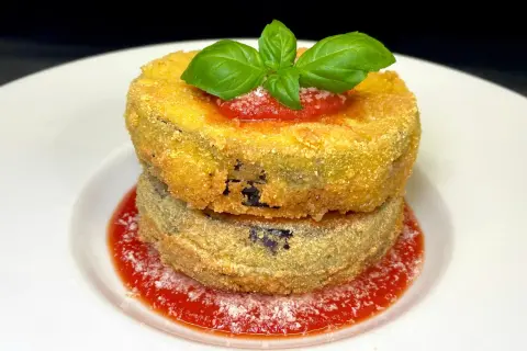 Due cordon bleu di melanzane impilati, dorati e croccanti, su un letto di salsa di pomodoro e basilico fresco.
