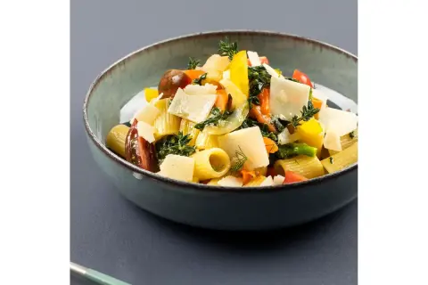 Piatto di pasta con verdure fresche, pomodorini, peperoni gialli e scaglie di parmigiano.
