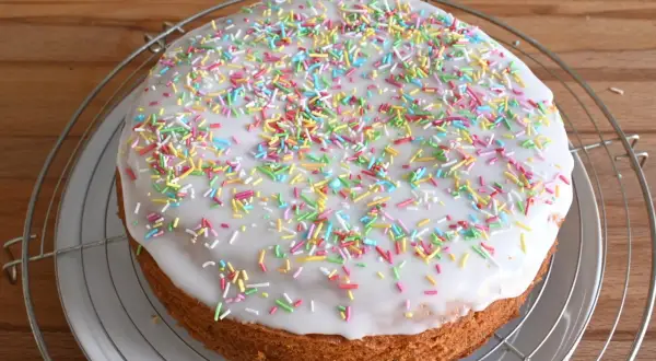 Torta rotonda con glassa di zucchero bianca e confettini colorati, su una griglia metallica.
