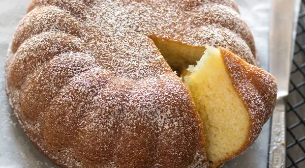 Una torta semplice e veloce, soffice e spolverata di zucchero a velo, con una fetta tagliata che ne mostra l'interno dorato.