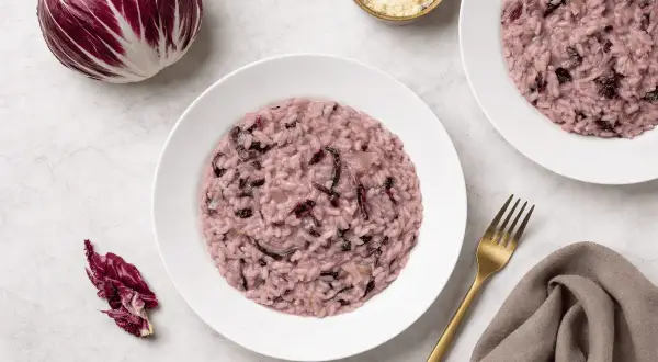 Un cremoso risotto al radicchio rosso, con un cespo intero e foglie sparse, pronto per essere gustato.