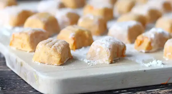 Gnocchi di zucca fatti in casa, morbidi e colorati, pronti per essere cucinati su un tagliere di legno.