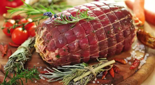 Un succulento arrosto di manzo, legato con spago e guarnito con rosmarino e lavanda, pronto per essere cucinato con pomodorini, peperoncini e carote.