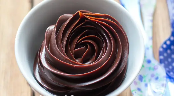 Una spirale perfetta di ganache al cioccolato, lucida e invitante, in una ciotola bianca.