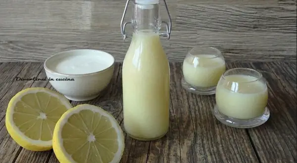 Una bottiglia e due bicchierini di crema di limoncello, con limoni freschi e una ciotola di panna.