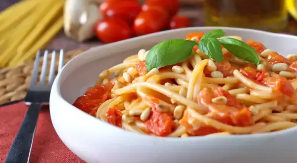 Un piatto invitante di spaghetti con pomodorini freschi, pinoli tostati e basilico, pronto per essere gustato.