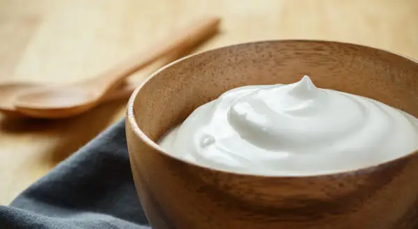 Una ciotola di legno piena di soffice crema al latte, pronta per essere gustata. Due cucchiai di legno sullo sfondo.
