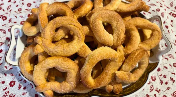 Un piatto pieno di torcetti al burro, dorati e zuccherati, pronti per essere gustati.