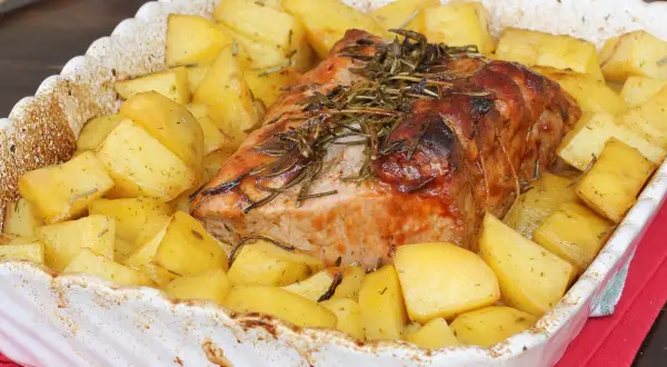 Arrosto di maiale succulento cotto al forno con patate dorate e rosmarino, un piatto invitante pronto per essere gustato.