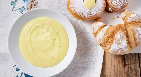 Una ciotola di crema pasticcera senza uova, perfetta per farcire croissant e bomboloni spolverati di zucchero a velo.