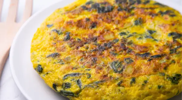 Frittata di spinaci dorata e soffice su un piatto bianco, con un utensile in legno sullo sfondo.