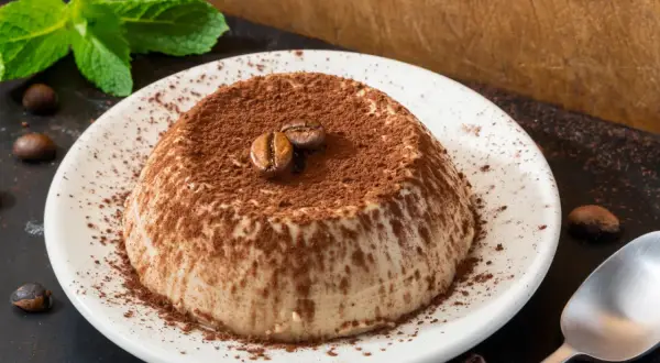 Deliziosa panna cotta al caffè, cosparsa di cacao e decorata con chicchi di caffè e menta fresca.