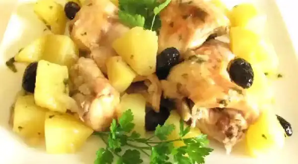 Coniglio in padella con patate e olive nere, guarnito con prezzemolo fresco. Un piatto saporito e invitante.