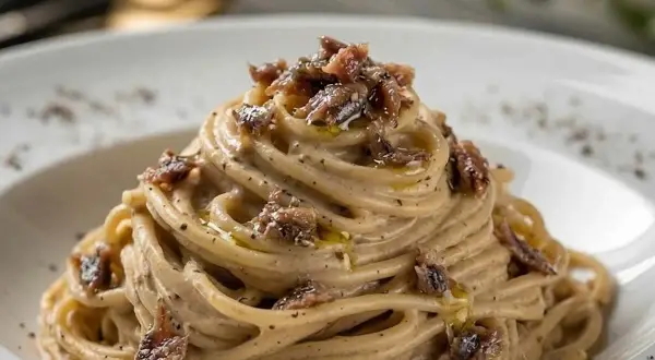 Spaghetti burro e alici, un piatto cremoso e saporito, con fili di pasta avvolti in una salsa delicata e guarniti con pezzetti di acciughe.