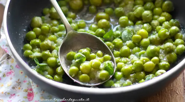 Piselli freschi in padella, cotti con cipolla e menta. Un cucchiaio ne raccoglie una porzione invitante.
