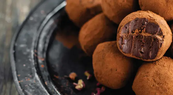 Un mucchio di tartufini al cioccolato ricoperti di cacao, uno aperto rivela il ripieno fondente.