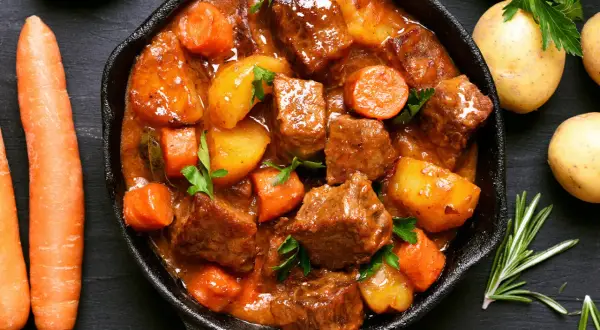 Un saporito spezzatino di maiale in padella con patate e carote, guarnito con prezzemolo fresco.