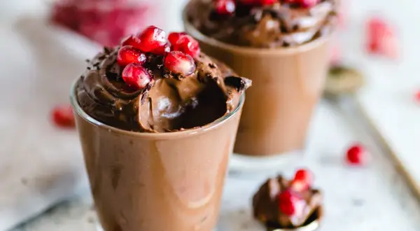 Due bicchierini di golosa mousse al cioccolato, guarniti con chicchi di melagrana e scaglie di cioccolato.