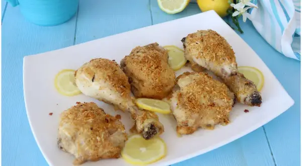 Cosce di pollo al limone croccanti e dorate, servite su un piatto bianco con fette di limone fresco.