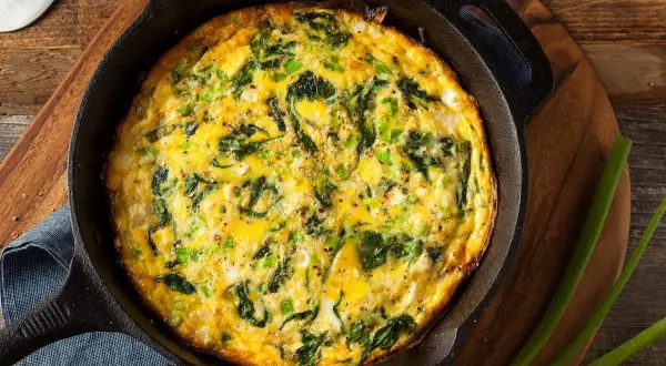 Frittata al forno con spinaci e cipollotti, appena sfornata in padella di ghisa, pronta per essere gustata.