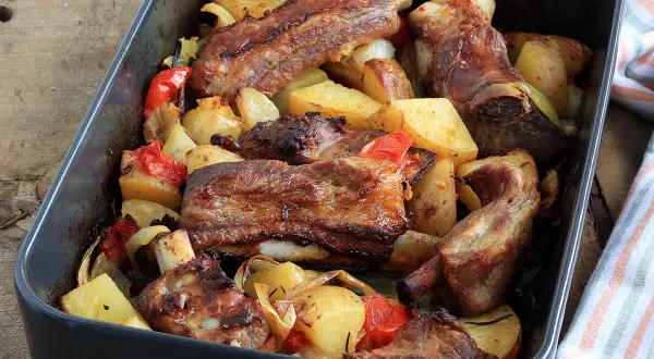 Puntine di maiale succulente al forno con patate, peperoni e cipolle in una teglia scura.