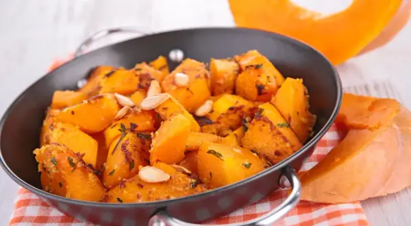 Zucca in agrodolce cotta in padella, guarnita con semi di zucca e erbe aromatiche. Un contorno autunnale saporito.