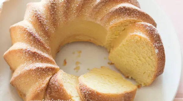 Una torta di ricotta sofficissima, dorata e cosparsa di zucchero a velo, tagliata a fette su un piatto bianco.