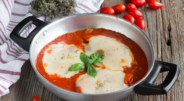 Un invitante pollo alla pizzaiola in padella, con mozzarella filante e basilico fresco, pronto per essere gustato.