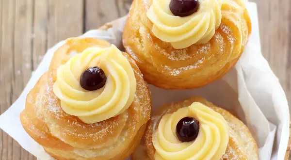 Tre zeppole di San Giuseppe, dolci fritti con crema pasticcera e ciliegina, spolverate di zucchero a velo.