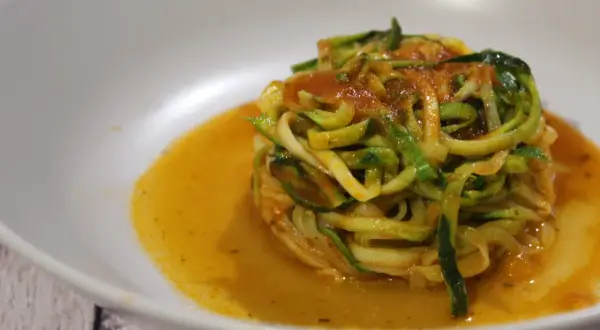 Un piatto di spaghetti di zucchine conditi con sugo rosso, serviti in una ciotola bianca.
