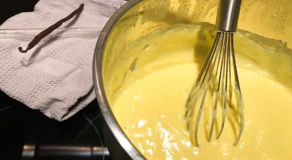 Crema pasticcera senza latte in preparazione, con bacca di vaniglia e frusta.