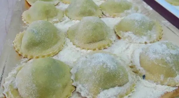 Un vassoio pieno di ravioli ricotta e spinaci freschi, spolverati di farina, pronti per essere cucinati.