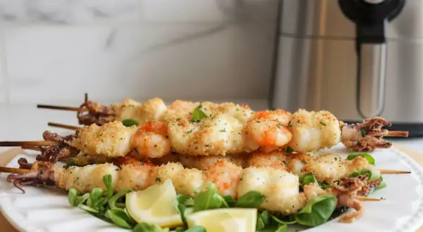 Spiedini di gamberi e calamari impanati, cotti alla perfezione nella friggitrice ad aria, serviti su un letto di insalata con spicchi di limone.