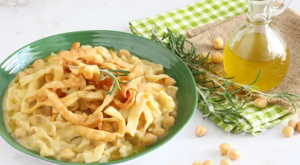Piatto di ciceri e tria, pasta fresca con ceci, guarnito con rosmarino e croccanti straccetti fritti. Olio d'oliva e ceci sparsi intorno.
