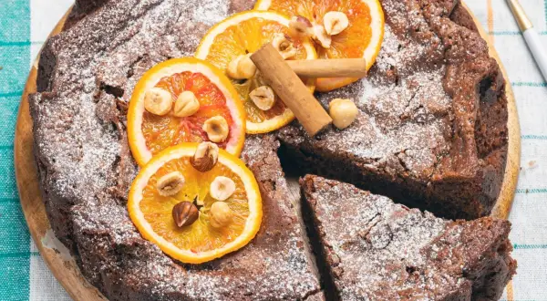 Torta di pane al cioccolato, decorata con fette d'arancia, nocciole e cannella, spolverata di zucchero a velo.