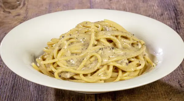 Un piatto di spaghetti cremosi al cacio e pepe, conditi con pepe nero macinato fresco.