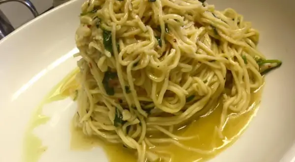 Un piatto di spaghetti aglio olio e peperoncino cremosi, conditi con prezzemolo fresco e un filo d'olio d'oliva, serviti in una ciotola bianca.