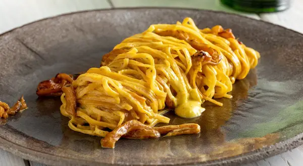Un piatto di spaghetti con funghi e una cremosa salsa gialla, un esempio di ricette pasta gustose che invitano a scoprire nuovi sapori.