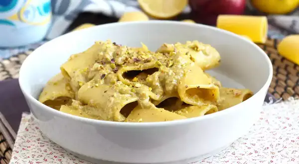 Un piatto di pasta in bianco condita con una crema di pistacchio e guarnita con granella dello stesso frutto secco.